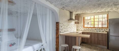 A bedroom with a canopy bed, a small kitchen with a stone countertop, and a refrigerator.