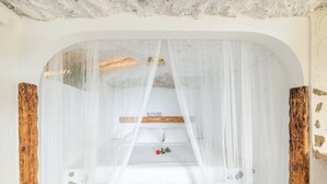 A room with a bed under a sheer canopy, a wooden headboard, and a stone-patterned floor.
