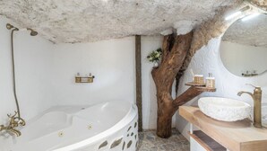 A bathroom with a large bathtub, a wooden tree trunk, a white sink, and a mirror.