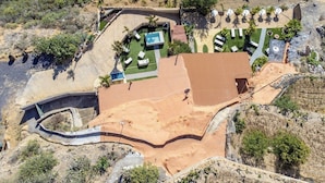 An aerial view of a resort with a swimming pool, sun loungers, and a landscaped garden.