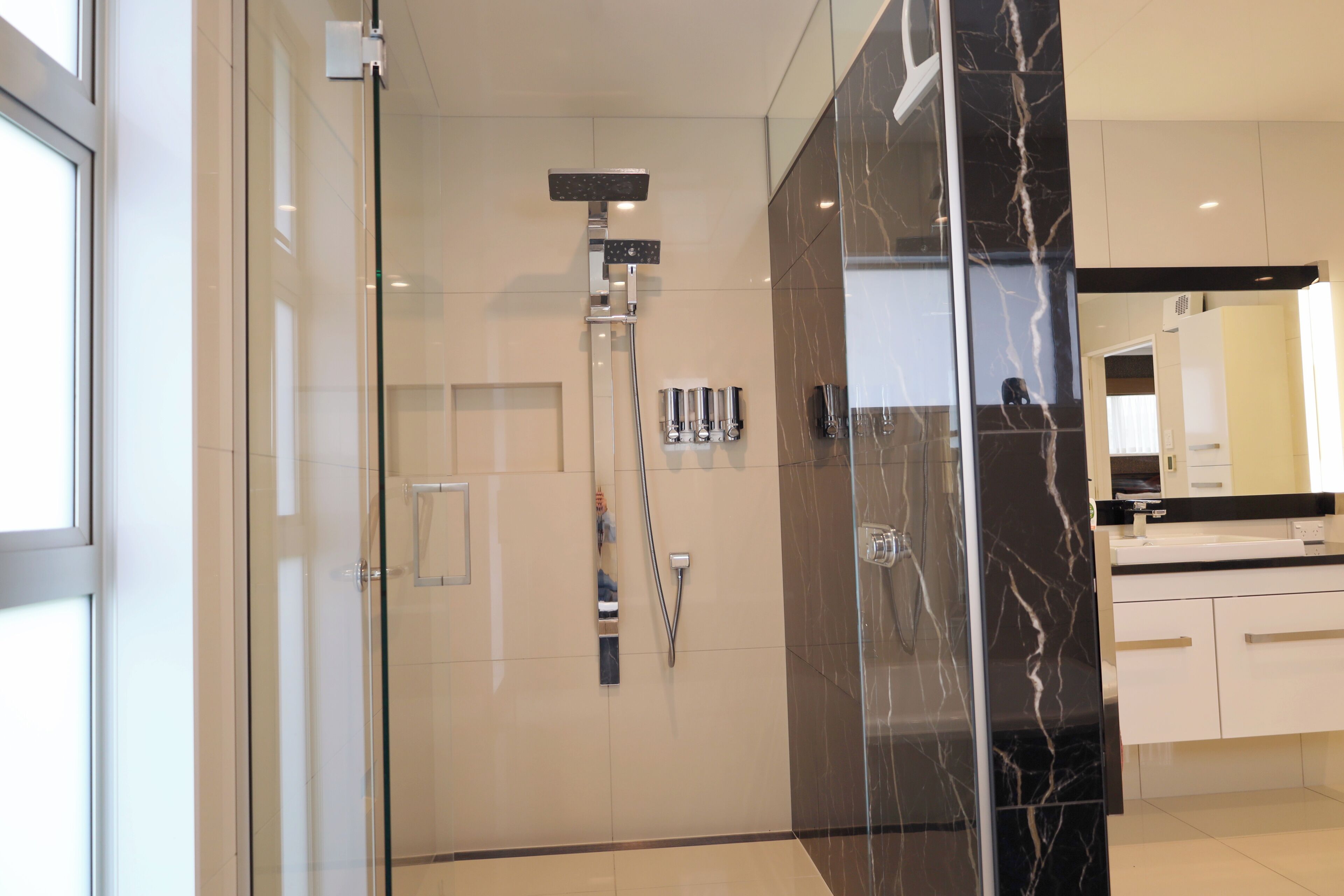 Een moderne badkamer met een douchecabine van glas, een marmeren wand en een wit aanrecht.