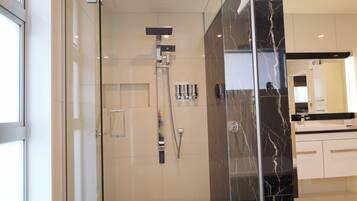 Een moderne badkamer met een douchecabine van glas, een marmeren wand en een wit aanrecht.