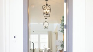 Une porte qui donne sur un salon, où l’on trouve un canapé, un tapis et un luminaire suspendu.