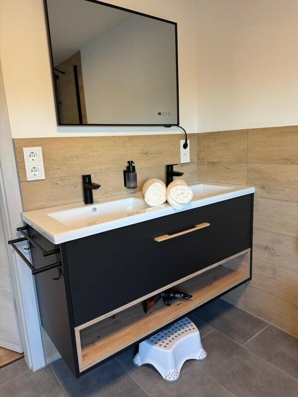 A modern bathroom with a double sink, a mirror, and a wooden vanity.
