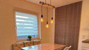 Un comedor con una mesa de madera, sillas blancas, un banco y lámparas colgantes.