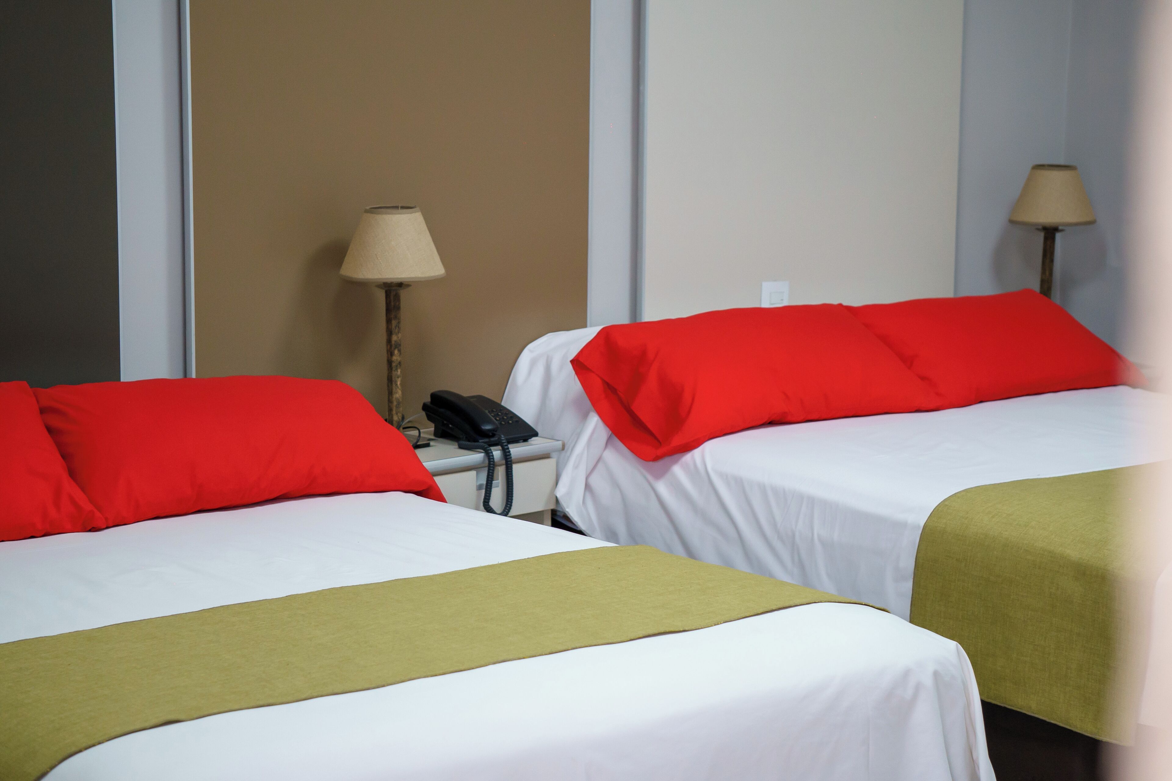 A hotel room with two beds, each with red and white bedding, a bedside telephone, and a lamp on a nightstand.