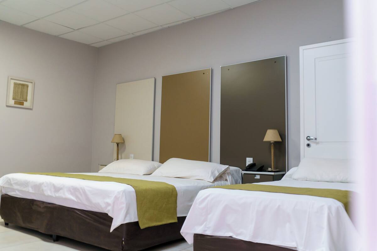 A hotel room with two beds, a large mirror, and a nightstand with a lamp.