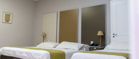 Una habitación de hotel con dos camas, un espejo grande y una mesita de noche con lámpara.