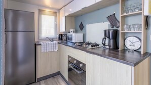A compact kitchen with a refrigerator, microwave, stove, and coffee maker. - Mobile Home 'Sur Pont-Aven' with Private Terrace, Garden, and Wi-Fi (Pont-Aven)