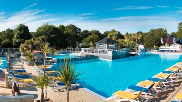 A large swimming pool with multiple lounge areas and a covered pavilion. - Mobile Home 'Sur Pont-Aven' with Private Terrace, Garden, and Wi-Fi (Pont-Aven)