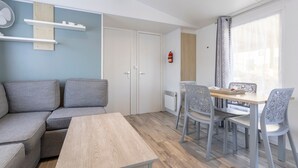 A modern living room with a sofa, dining table, and chairs, a fan, and a fire extinguisher. - Mobile Home 'Sur Pont-Aven' with Private Terrace, Garden, and Wi-Fi (Pont-Aven)