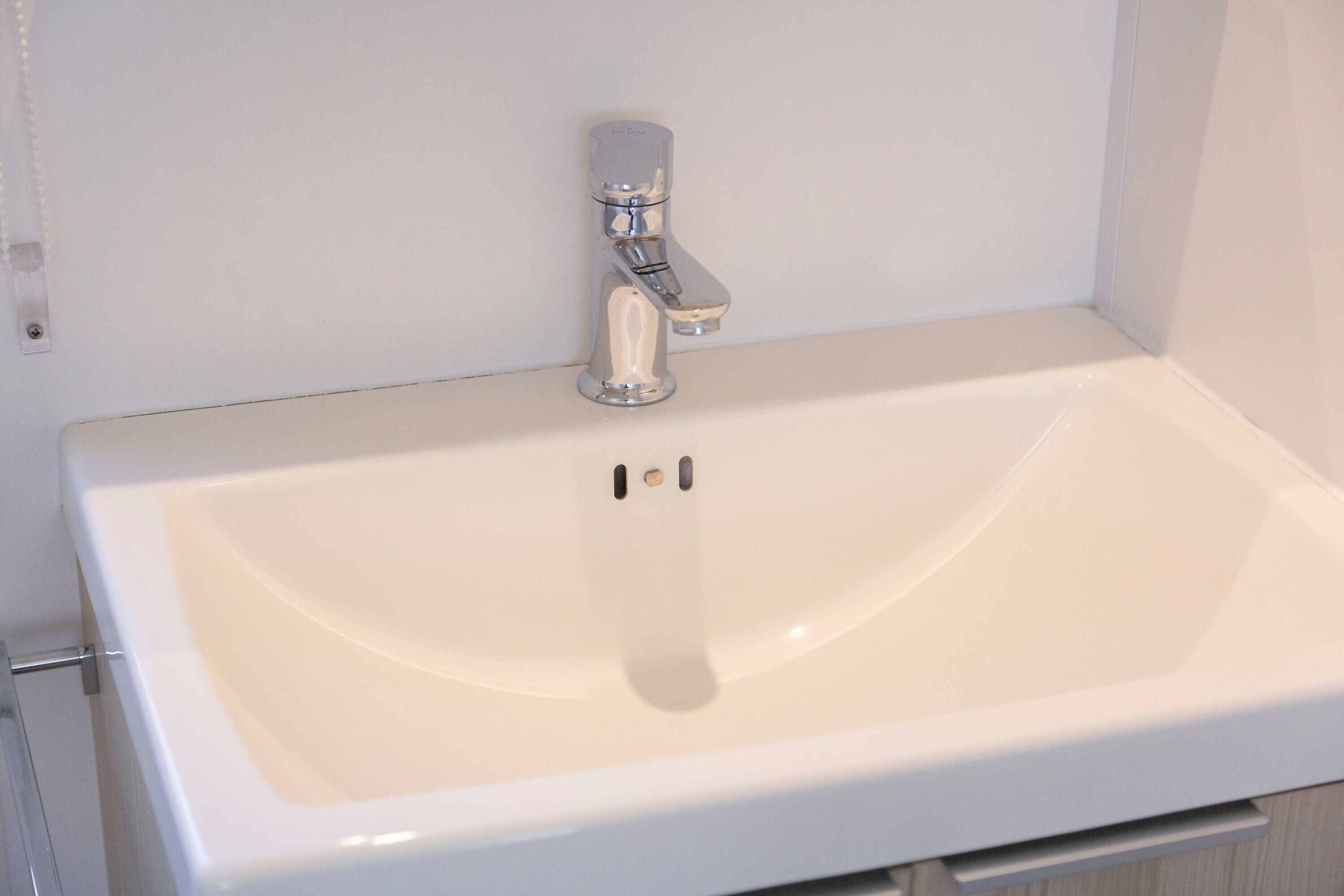A white bathroom sink with a chrome faucet, a mirror above it, and a towel rack to the left.