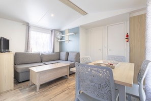 Una habitación moderna y bien iluminada con un sofá, una mesa de centro, una mesa de comedor con sillas, un televisor y un extintor.