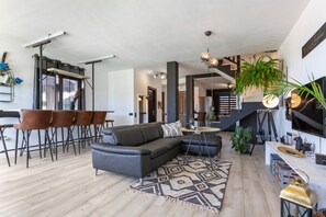 Ein modernes Wohnzimmer mit einer Eckcouch, einem Essbereich mit Stühlen, einer Treppe und einer großen Pflanze.
