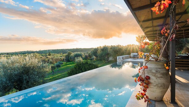 An infinity pool with a clear view of the surrounding landscape, including trees and a distant hill.