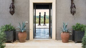 A doorway with two large potted plants on either side, leading to a view of two statues outside.
