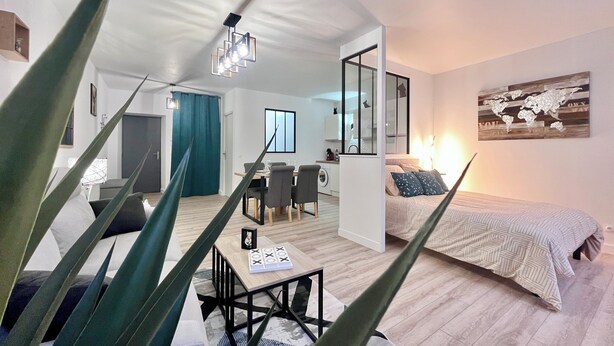 Un apartamento moderno con comedor, una cama y una planta grande al frente.
