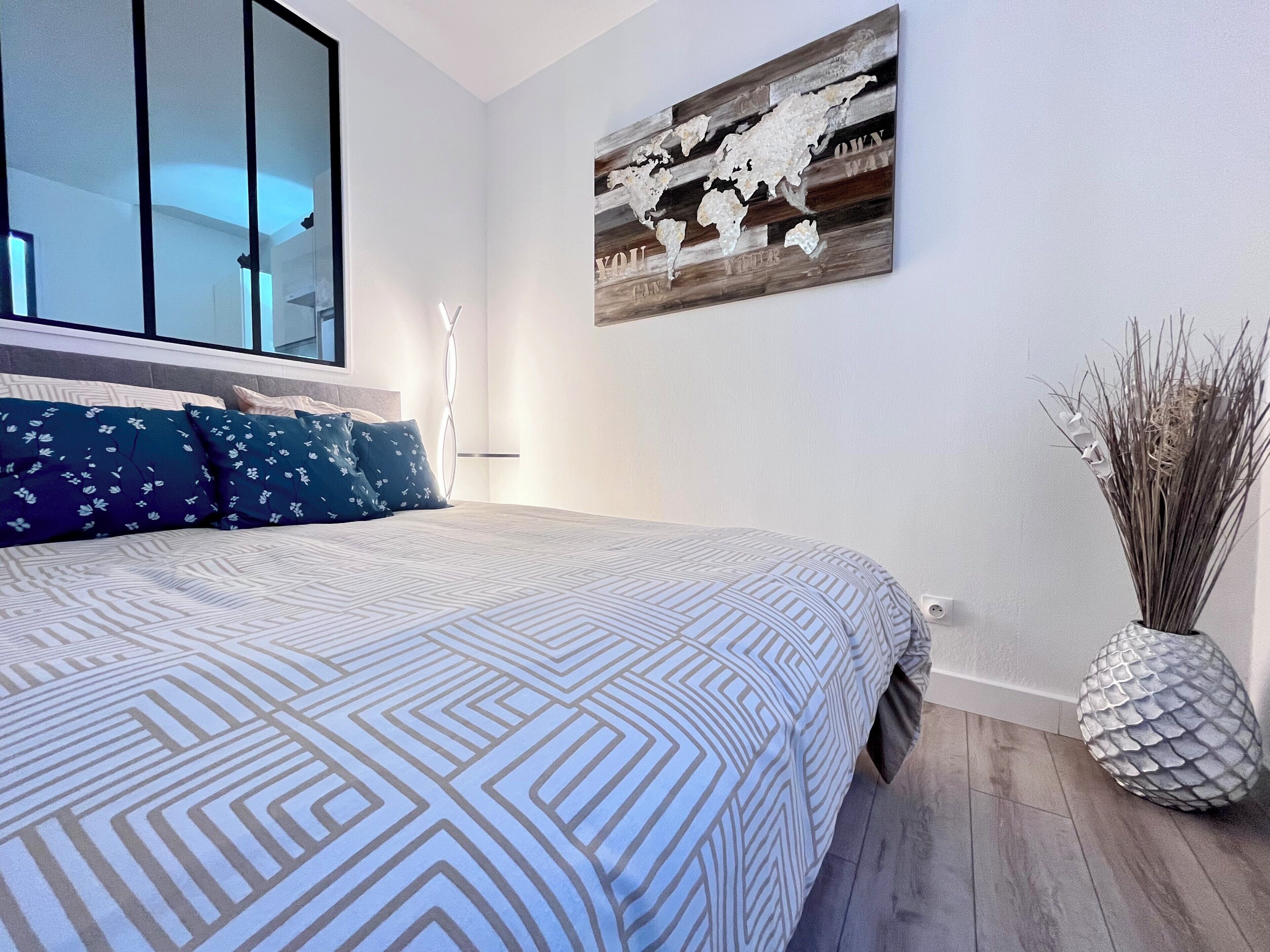 A bedroom with a large bed, a world map artwork, and a decorative vase.