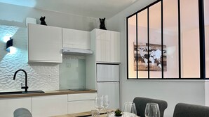 Una cocina moderna con armarios blancos, un grifo negro y una encimera de madera. Hay una mesa de comedor con platos, vasos y cubiertos.