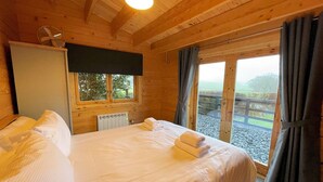 Een houten slaapkamer met een bed, een radiator, een raam en uitzicht op de natuur.