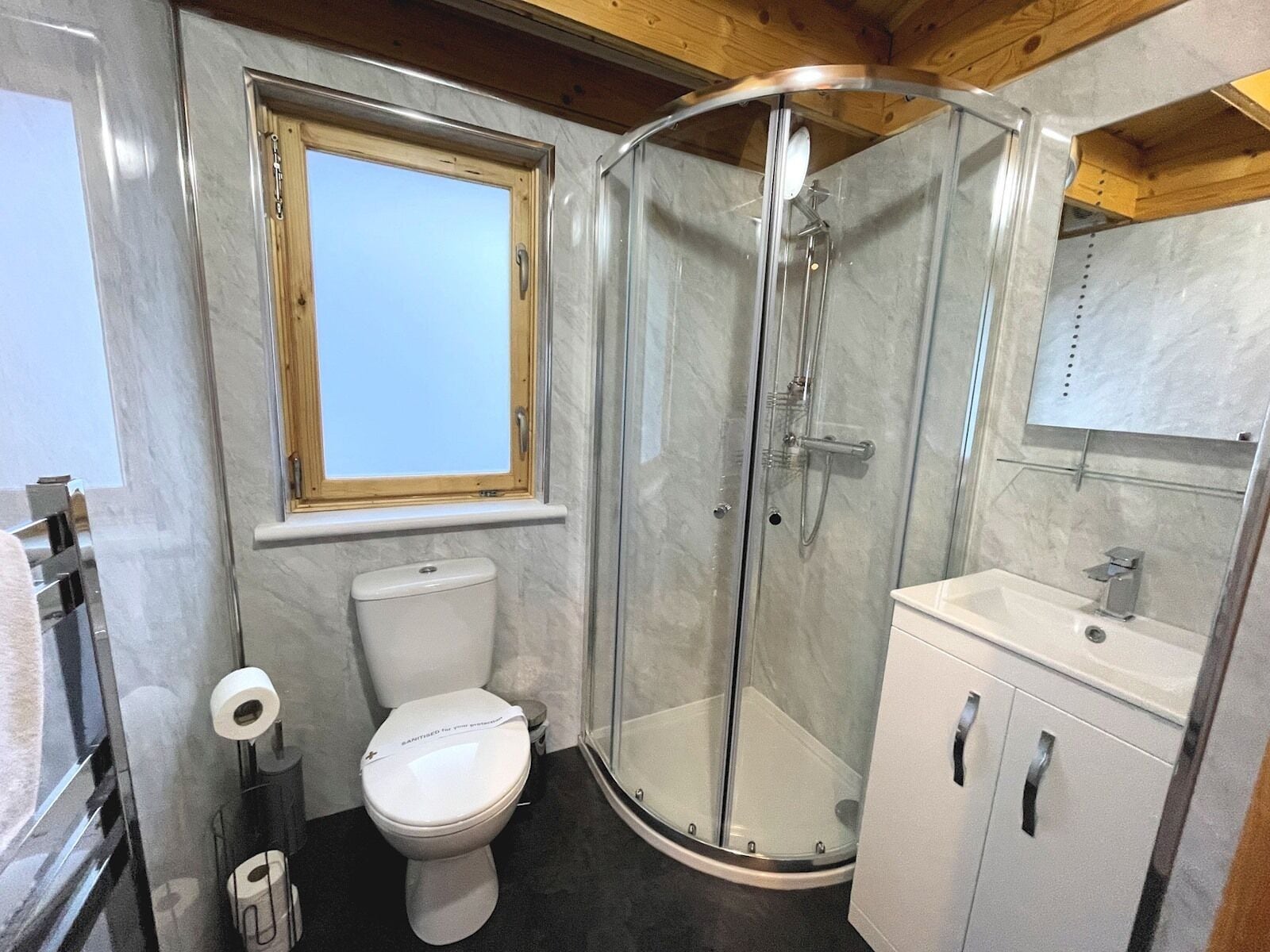 Ein modernes Badezimmer mit Duschkabine, Toilette, Waschbecken und Fenster.