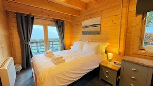 Een slaapkamer in een houten blokhut, met een bed, nachtkastjes en een raam met gordijnen.