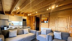 Een gezellig chaletinterieur met een moderne keuken, twee banken en een grote houten deur.