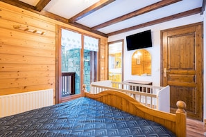 A wooden-paneled room with a bed, a stone wall, a television, and a wooden door. - Chalet 'Genepi - 14p' with Mountain Views, Private Terrace, and Wi-Fi (Les Belleville)