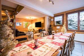 A cozy room with a wooden interior, a dining table with a quilt, a Christmas tree, and a fireplace. - Chalet 'Genepi - 14p' with Mountain Views, Private Terrace, and Wi-Fi (Les Belleville)