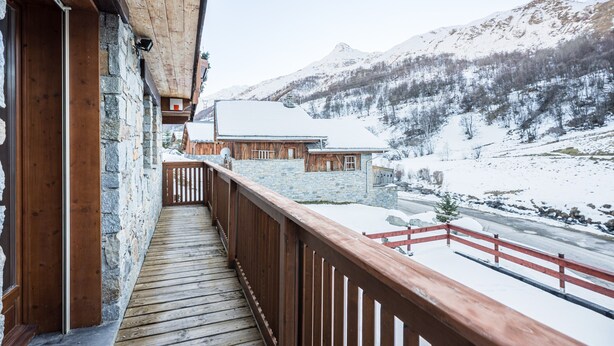 A wooden balcony with a stone wall, a wooden deck, and a view of snow-covered mountains.