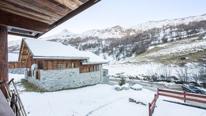 A wooden cabin with a stone foundation, a snow-covered roof, and a view of snow-covered mountains.