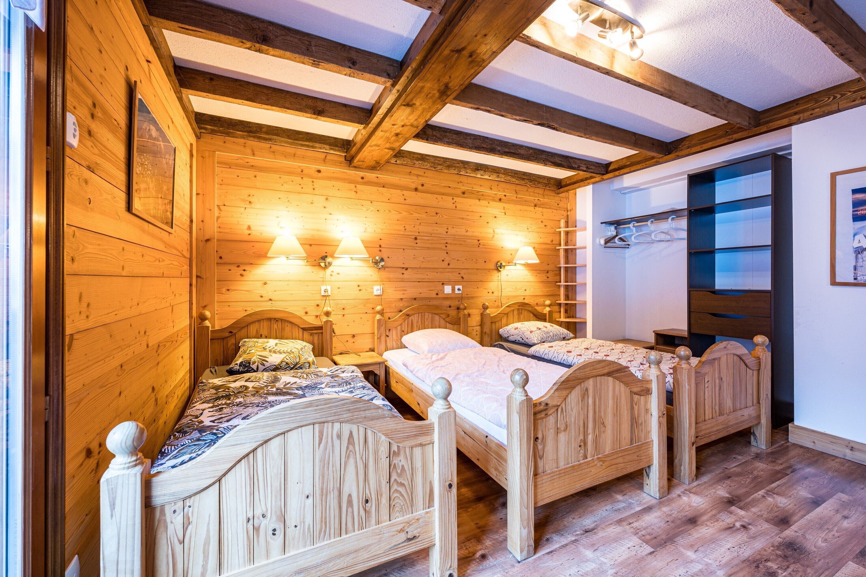 A wooden room with two beds, wooden beams on the ceiling, and wall-mounted lights.