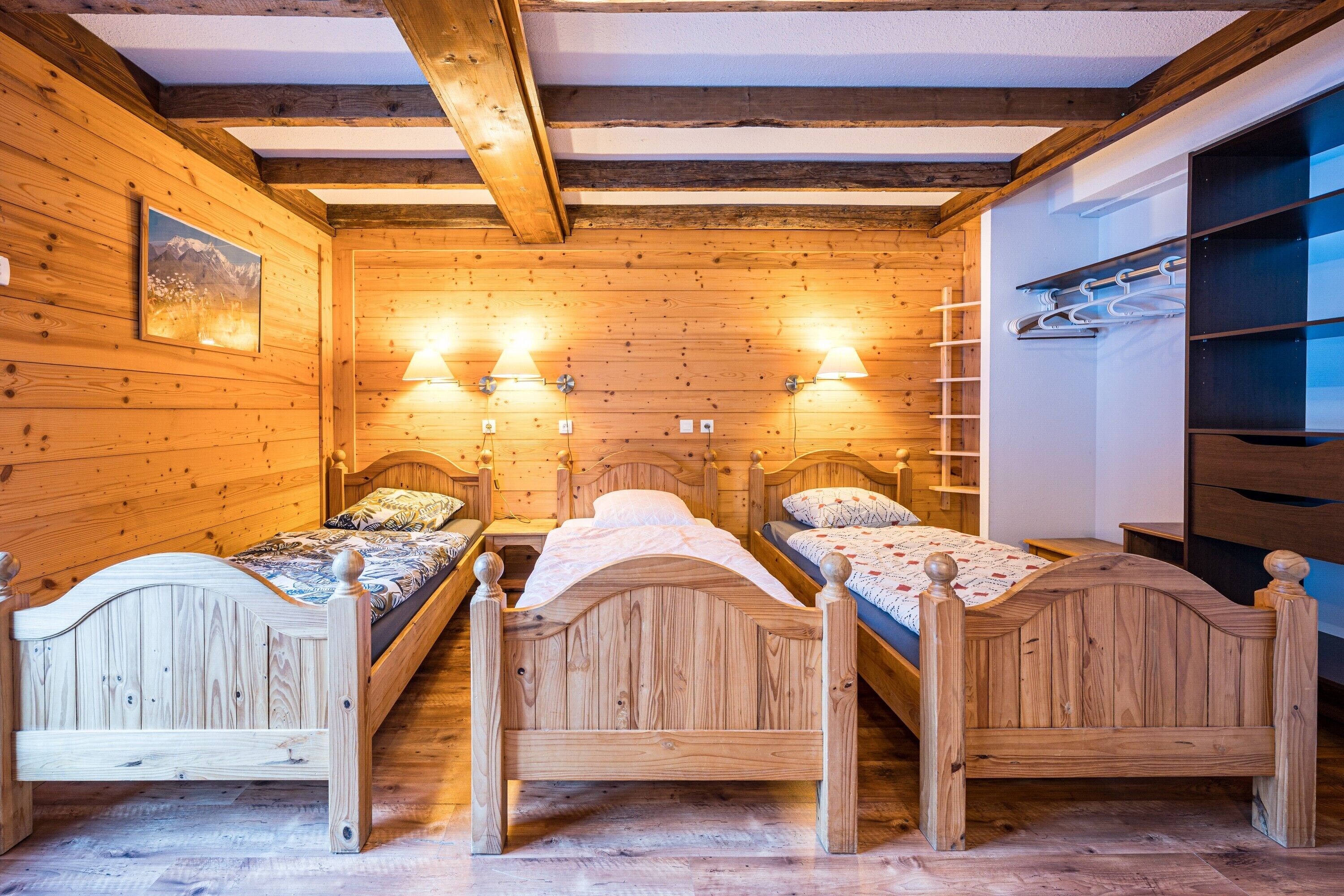 Een houten kamer met drie bedden, houten balken in het plafond en een plank aan de muur met kleding.