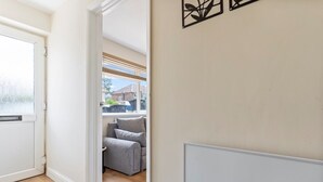A hallway with a grey sofa, a white radiator, and a window with blinds. - Lovely flat near Gatwick Airport with free parking  (Surrey)