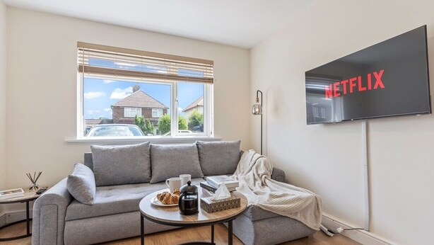 A modern living room with a grey sofa, a coffee table, and a TV mounted on the wall displaying the Netflix logo. - Lovely flat near Gatwick Airport with free parking  (Surrey)