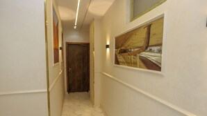 Um corredor com paredes brancas, uma porta de madeira no fim e um quadro de barco na parede.