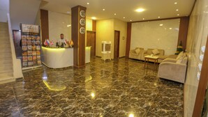 Uma área de recepção de hotel com piso de mármore, balcão de atendimento, sofá e relógio fixado na parede.