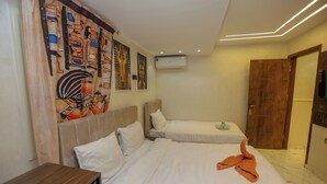 Quarto de hotel com duas camas, cabeceira de madeira, ar condicionado fixado na parede e uma porta.