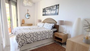 Une chambre à coucher avec un lit, des tables de chevet, un miroir, une lampe, un tableau au mur et une fenêtre.