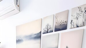 Une console en bois ornée de motifs géométriques, un tapis tissé et un mur sur lequel sont accrochées plusieurs peintures de paysages.