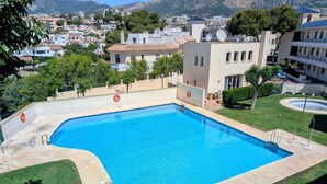 Une piscine rectangulaire à l’eau d’un bleu limpide, entourée d’une terrasse dallée et bordée d’une pelouse parsemée d’arbres.