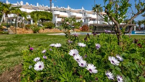 A garden with white and purple flowers in the foreground, a pool in the background, and a row of white buildings with balconies. - Apartment 'Calahonda Park' with Sea View, Wi-Fi and Air Conditioning (Calahonda)