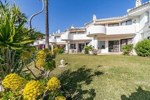 A white building with balconies, a well-maintained lawn, and tropical plants.