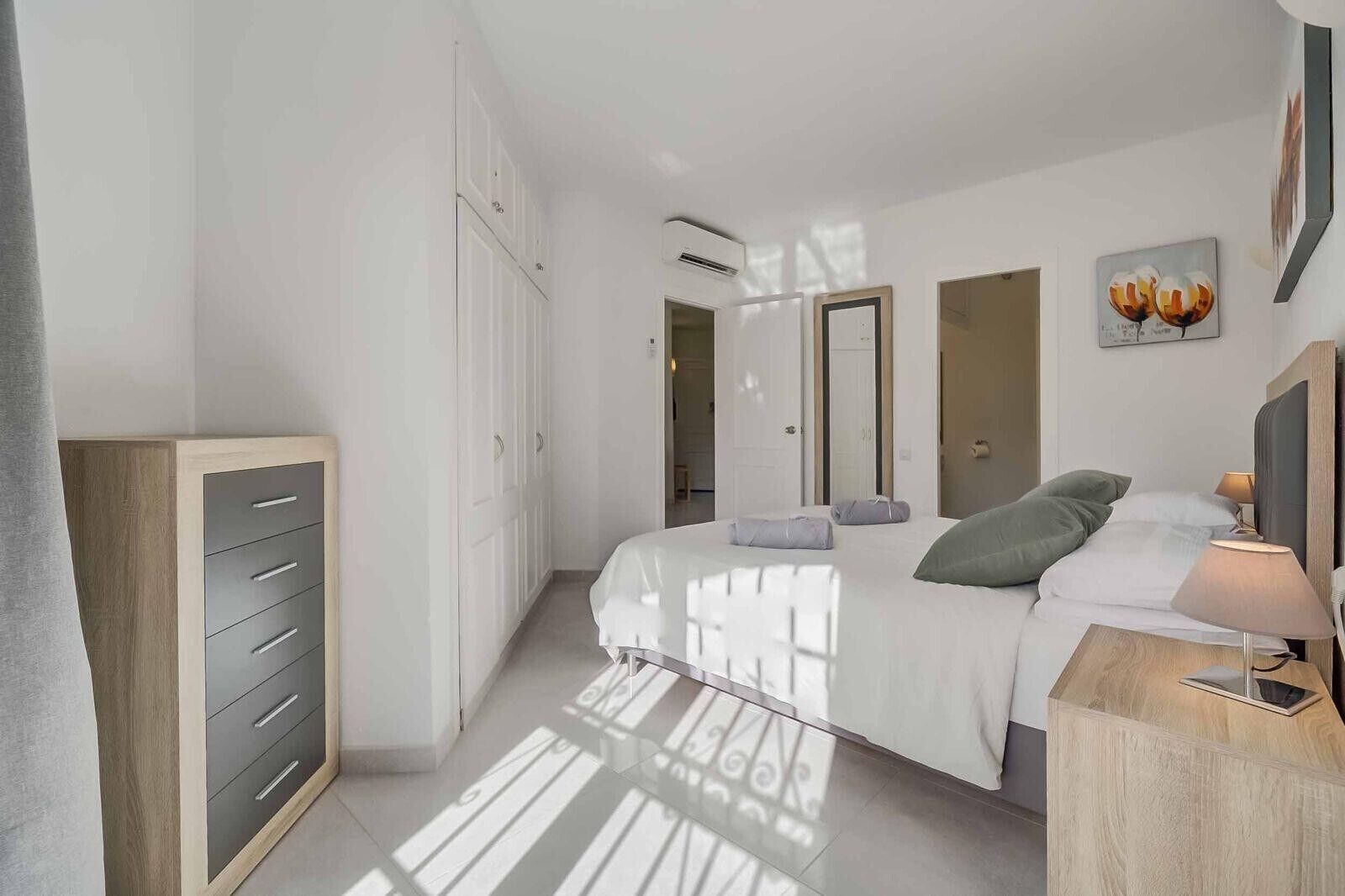 Une chambre à coucher avec un lit, une table de chevet, une lampe, une armoire et un tableau accroché au mur.