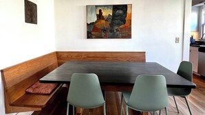 Un comedor con un banco de madera, una mesa oscura y cuatro sillas verdes.