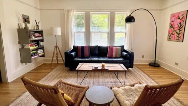 Una sala de estar con un sofá de cuero negro, dos sillones de mimbre, una mesita redonda y una lámpara de pie.