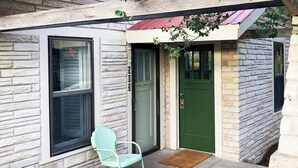 Una casa de piedra con puerta verde, una ventana y una silla azul claro en el exterior.