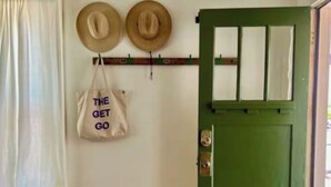 Una puerta verde con una ventana, dos sombreros en un perchero de pared y un bolso con texto.