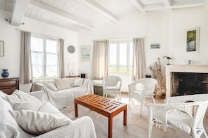 Een woonkamer met een open haard, rieten meubels en uitzicht op de omgeving.