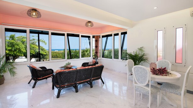 A spacious room with a large window, a dining area with a table and chairs, and a seating area with wicker furniture.